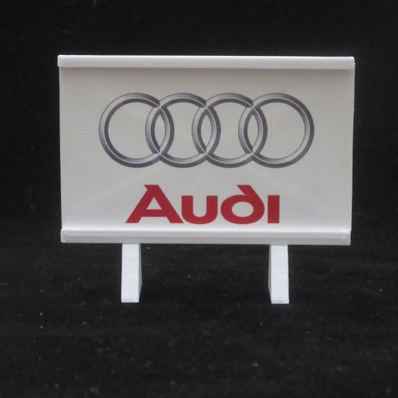 May include: A white sign with a red Audi logo and four interlocking rings. The sign is on two white stands.