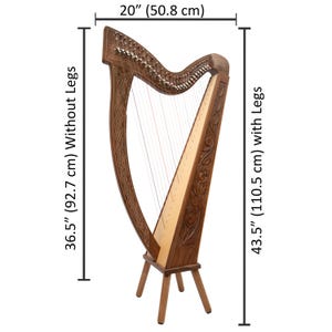 May include: A brown wooden harp with intricate carvings. The harp is 36.5 inches (92.7 cm) tall without legs and 43.5 inches (110.5 cm) tall with legs. It is 20 inches (50.8 cm) wide. The harp has strings and is set on a three-legged stand.