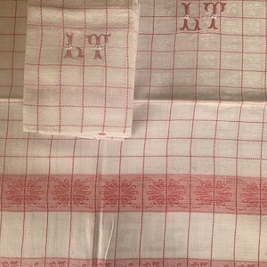 May include: Two white linen tea towels with pink checkered patterns and embroidered initials "LM" and "YM". The towels have a pink border with a floral design.