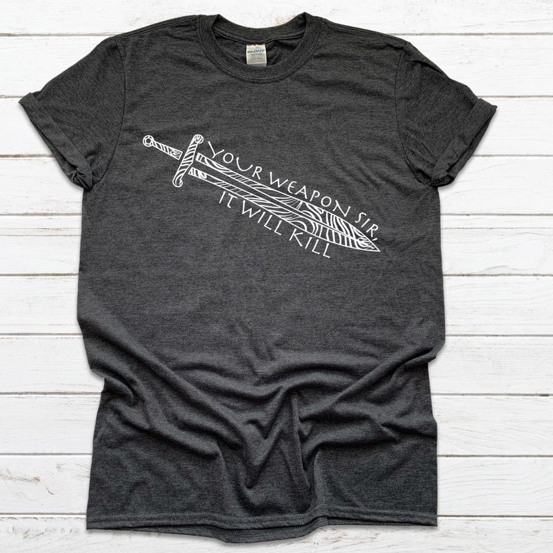 May include: A dark heather grey t-shirt with a white graphic of a sword and the text "Your Weapon Sir It Will Kill."