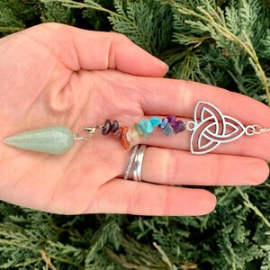 May include: A green crystal pendulum with a silver chain and a silver Celtic knot charm. The chain is adorned with small, colorful crystals in a rainbow pattern.