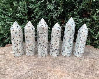 May include: Seven white and gray speckled granite crystal points arranged in a row on a wooden surface.