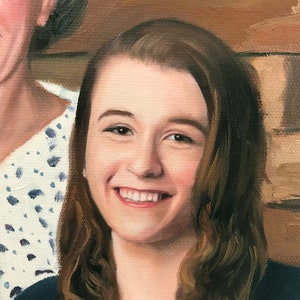 May include: A close-up portrait of a young woman with long brown hair smiling. She is wearing a dark blue shirt and is standing next to an older woman.