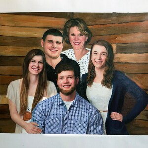 May include: A painting of a family of five, including two women, two men, and one young woman. The family is posed in front of a wooden wall. The women are wearing white shirts, and the men are wearing blue shirts. The young woman is wearing a blue sweater.