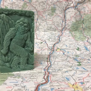 Puede incluir: Una pastilla de jabón verde con una imagen en relieve de una criatura parecida a Bigfoot en un entorno boscoso.