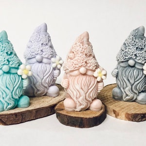 May include: Four handmade gnome figurines with floral details on their hats and beards. Each gnome is holding a small white flower and is standing on a wooden base.