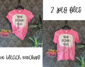 Könnte beinhalten: Zwei rosa T-Shirts, die mit Bleichmittel behandelt wurden, mit dem Text "YOUR DESIGN HERE" in Schwarz. Die Shirts befinden sich auf einem gemusterten Hintergrund mit einer Pflanze in der Ecke.