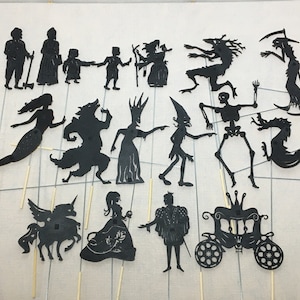 Könnte beinhalten: Ein Set mit 17 schwarzen Schattenpuppen, darunter eine Meerjungfrau, ein Wolf, eine Hexe, ein Skelett, ein Drache, ein Einhorn, eine Prinzessin, ein Prinz und eine Kutsche. Die Puppen sind aus Pappe und an Stöcken befestigt.