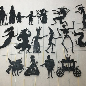 May include: A set of 17 black silhouette puppets, including a mermaid, a wolf, a unicorn, a princess, a prince, a dragon, a skeleton, a witch, a carriage, and more. The puppets are made of black cardstock and are attached to wooden sticks.