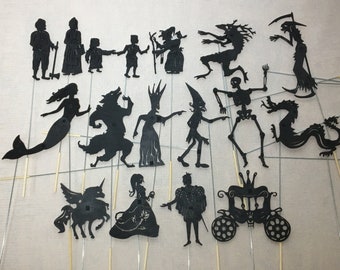 May include: A set of 17 black silhouette puppets, including a mermaid, a wolf, a unicorn, a princess, a prince, a dragon, a skeleton, a witch, a carriage, and more. The puppets are made of black cardstock and are attached to wooden sticks.