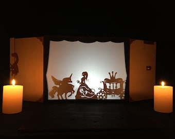 May include: A shadow puppet theater with a white screen lit by two candles. The screen shows a silhouette of a princess, a unicorn, and a carriage.