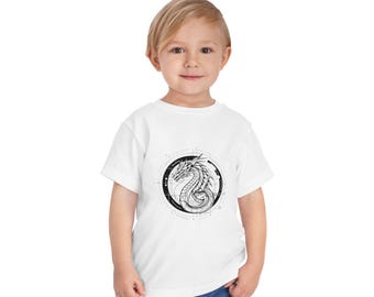 May include: White t-shirt with a black and white graphic of a dragon in a circle on the front.