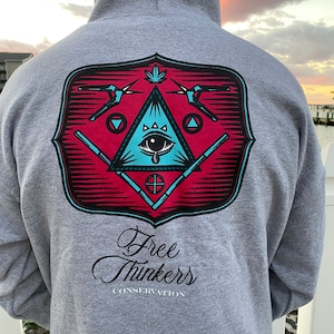 May include: A gray hooded sweatshirt with a red and blue graphic on the back. The graphic features a stylized eye with a tear, a triangle, and a marijuana leaf. The text "Free Thinkers Conservation" is printed below the graphic.
