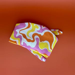 May include: A pink, yellow, and orange patterned fabric headband with a swirl design.