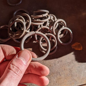 May include: A pile of metal rings, some are stacked on top of each other, and one is being held by a hand. The rings are a dull silver color and appear to be made of metal.