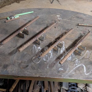 May include: Five metal rods with rings on one end and multiple metal pieces attached to the other end. The rods are laying on a metal workbench.