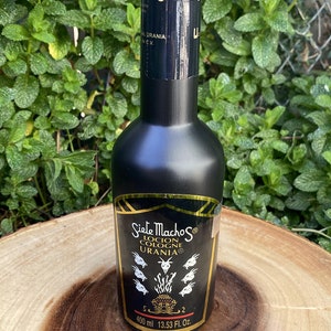 May include: A black cologne bottle with gold lettering and a label featuring the text "Siete Machos Locion Cologne Urania". The bottle contains 400 ml or 13.53 fl oz of cologne. The bottle is set against a green leafy background.