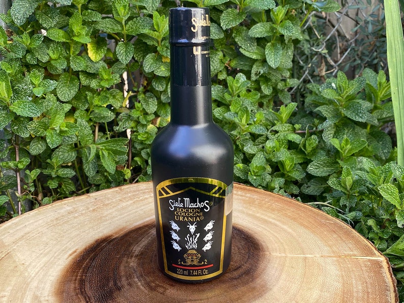 May include: A black cologne bottle with gold accents and the text "Siete Machos Locion Colonia Urania." The bottle has a black cap and a gold label with a detailed illustration. The bottle contains 7.44 fl oz (220 ml).