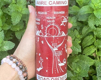 May include: A tall red cylindrical glass candle featuring white printed text and graphics. The label displays the words ABRE CAMINO and ROAD OPENER, along with symbols for money, health, business, love, and a sun rising over a road.
