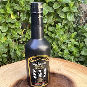 May include: A black cologne bottle with a gold label featuring the text "Siete Machos Locion Cologne Urania". The bottle contains 7.44 fl oz (220 ml) of cologne. The background is a green leafy plant.