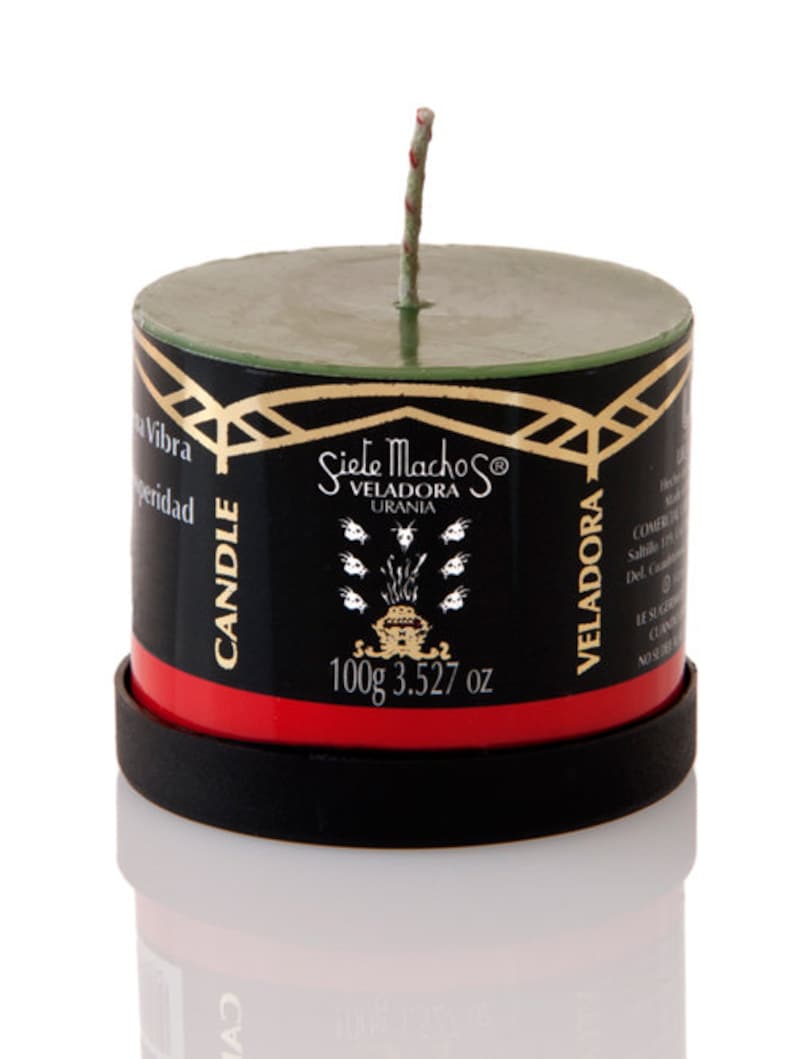 May include: A cylindrical candle with a green top and a black body, featuring gold accents and the text "Siete Machos Veladora Urania." The candle has a red band and a black base. It weighs 3.527 oz.
