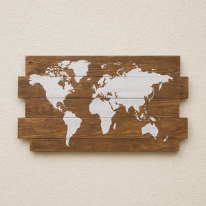 Peut inclure: Carte du monde en bois. La carte est peinte en blanc sur un fond de planches de bois teinté. Le bois a un grain naturel et est assemblé en rangées horizontales. La carte représente les continents et les océans.