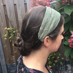 May include: A woman with brown hair wearing a green lace headband. She is wearing a black and floral print blouse.