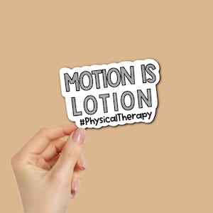 May include: A white sticker with the text "MOTION IS LOTION" in black, outlined in black. Below the text is the hashtag "#PhysicalTherapy". The sticker is held by a hand against a tan background.
