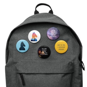 May include: A gray backpack with five round buttons attached to it. The buttons have different images and text. One button has a silhouette of a horse with the text "What is this, a crossover episode?" Another button has a silhouette of a horse with the text "You turn yourself around. That's what it's all about." Another button has a silhouette of a horse with the text "The only thing that matters is right now. This moment." Another button has a silhouette of a horse with the text "What is this, a crossover episode?" Another button has a silhouette of a horse with the text "What is this, a crossover episode?"