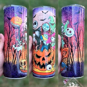 May include: A stainless steel tumbler with a colorful design featuring characters from the Nightmare Before Christmas. The design includes Jack Skellington, Sally, Oogie Boogie, and other characters from the film. The tumbler has a glittery purple and pink background with a black silhouette of trees and a full moon.