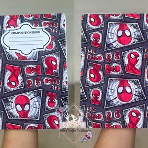 May include: Composition book featuring a repeating pattern of Spider-Man's face and head in red and black. The notebook has a black spine and the words "COMPOSITION BOOK" on the front.