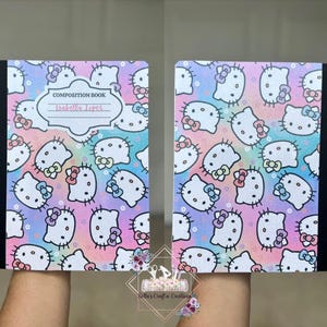 May include: Composition book featuring a colorful pattern of Hello Kitty characters on a pastel rainbow background. The cover includes the text "COMPOSITION BOOK" and a space for a name. The book has a black spine.