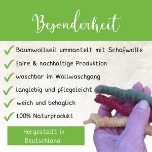 May include: A close-up of a hand holding four colorful cords made of cotton and wool. The cords are labeled with the text "Besonderheit" and a list of features, including "Baumwollseil ummantelt mit Schafwolle", "faire & nachhaltige Produktion", "waschbar im Wollwaschgang", "Langlebig und pflegeleicht", "weich und behaglich", "100% Naturprodukt", "Hergestellt in Deutschland".