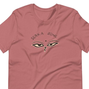 May include: A maroon t-shirt with a black and white graphic of a pair of eyes with the text "SERKA ZONG" above the eyes.