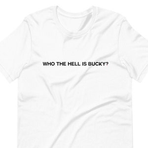 Pode incluir: Camiseta branca com o texto "WHO THE HELL IS BUCKY?" impresso em preto.