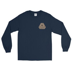 Puede incluir: Camiseta de manga larga azul marino con un pequeño parche beige de "Engineer" en el pecho. El parche presenta un diseño geométrico con la palabra "ENGINEER" debajo. La camiseta está hecha de un material suave.