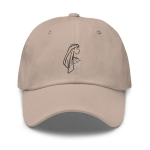 Puede incluir: Una gorra de béisbol beige con un diseño bordado de una mujer con el pelo largo que lleva un cubrecabezas. La mujer está de perfil y lleva un collar azul.