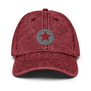 May include: A red vintage baseball cap with a gray and red star design. The star is in the center of the cap and is surrounded by a gray circle.