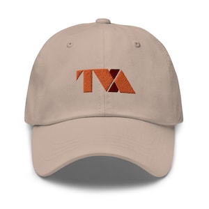 Può includere: Un cappello da baseball beige con un logo ricamato delle lettere "TVA" in arancione e rosso.