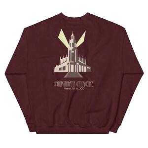 Puede incluir: Sudadera color burdeos con un gráfico blanco de un edificio con una alta aguja y el texto "Carthay Circle Anaheim, CA est 2012"