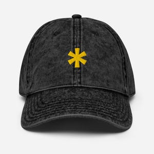 Puede incluir: Una gorra de béisbol de mezclilla vintage negra con un asterisco amarillo bordado en la parte delantera.