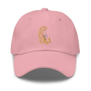 May include: A pink baseball cap with an embroidered image of a woman with long blonde hair. The woman is wearing a dress and holding a flower.