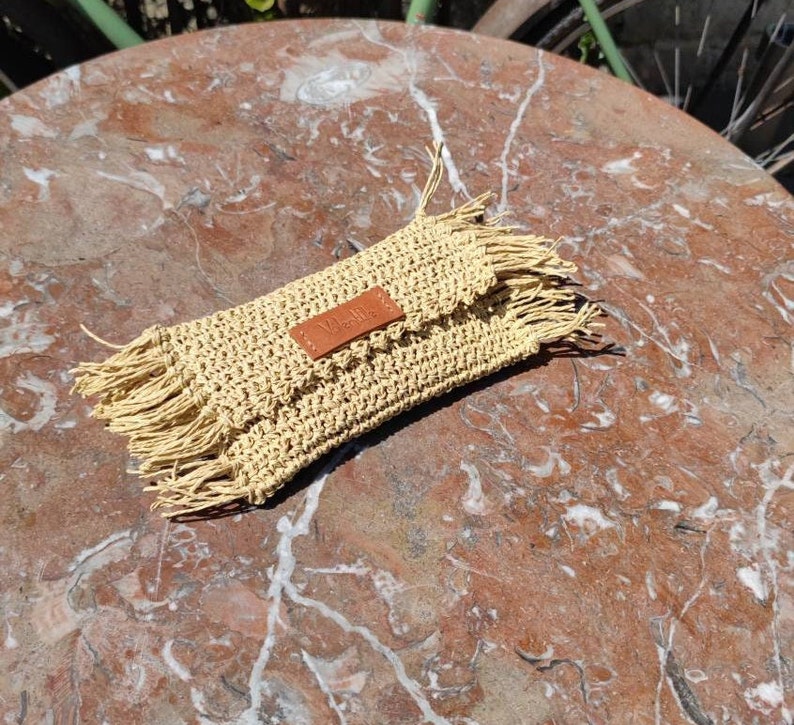May include: A beige crocheted clutch with a brown leather tag that says "Nella" and fringe details.