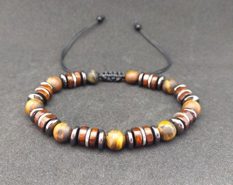 May include: A brown and gold beaded bracelet with a black cord closure. The bracelet features alternating tiger's eye and hematite beads.