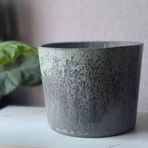May include: A gray concrete planter with a light green glaze. The glaze has a mottled, textured appearance.