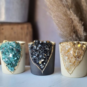 May include: Three small candle holders with gold trim and a crystal-like design. The holders are in teal, black, and white.