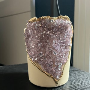 May include: A white ceramic planter with a gold rim and a purple crystal design. The planter is shaped like a geode and has a rough, textured surface.