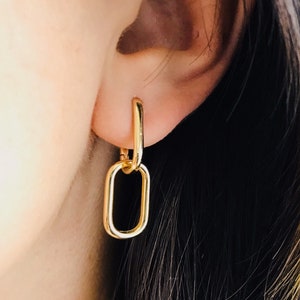 Könnte beinhalten: Goldene Kettenohrringe mit rechteckiger Form. Die Ohrringe werden am Ohr einer Person getragen.