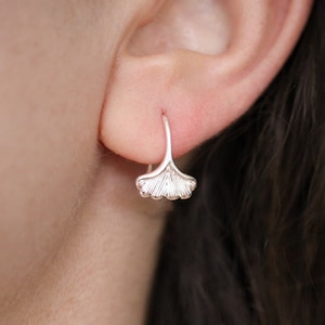 Puede incluir: Pendientes de plata con forma de hoja de ginkgo con un diseño delicado. Los pendientes son pequeños y simples, lo que los convierte en un accesorio perfecto para el día a día.
