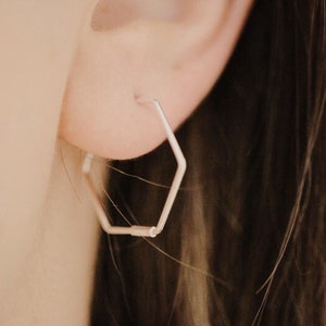 Puede incluir: Pendientes de aro hexagonales de plata. Los pendientes son simples y modernos, y serían una gran adición a cualquier colección de joyas.